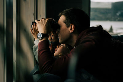 Father and daughter looking out the window with binoculars at nature