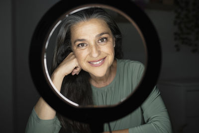 Smiling beautiful woman seen through ring light in darkroom