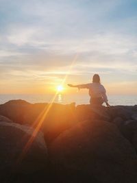 Man on rock against sky during sunset