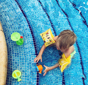 Top view of little boy play with plastic water toys in at swimming pool, wearing inflatable armbands