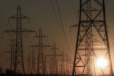 Low angle view of electricity pylon against sky during sunset