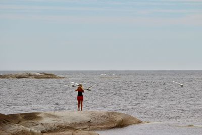 Birds flying over woman at beach against sky