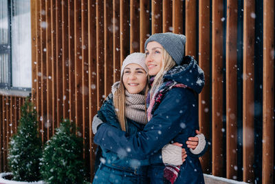 Two women girlfriends standing and cuddling rejoice in the snowy weather.