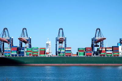 Cranes at harbor against clear sky