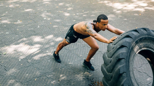 Full length of man lifting up tire on footpath