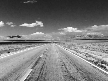 Empty road amidst field against sky