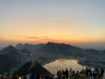 Group of people in city against sky during sunset