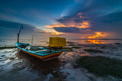 Boat moored on beach against sky during sunset