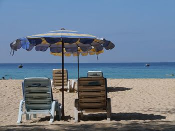 Deck chairs with umbrellas at beach against clear sky