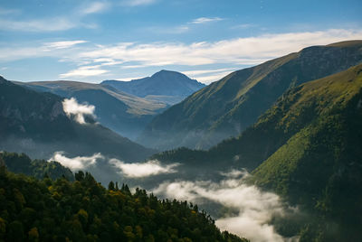 A mountain gorge with fog, a rock peak in the background and a blue sky with clouds and stars