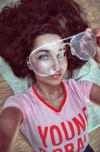 Close-up high angle portrait of woman holding eyeglasses while lying at home