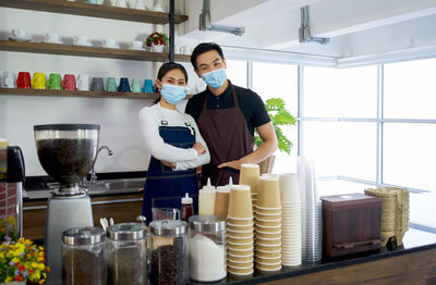 Portrait of smiling couple wearing mask standing at kitchen
