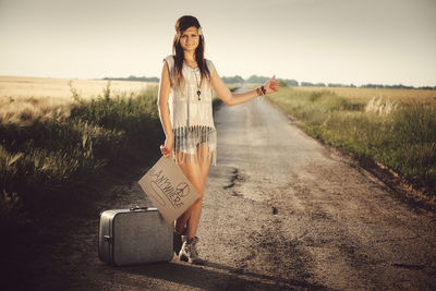 Full length portrait of woman hitchhiking while holding text on road