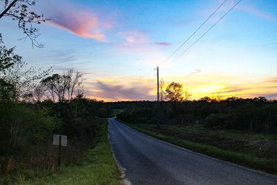 Road by trees against sky during sunset