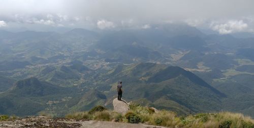 Rear view of man standing on rock at mountain peak