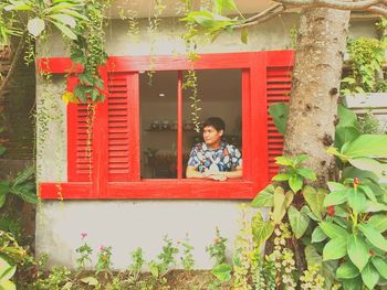 Portrait of boy with red plants against window