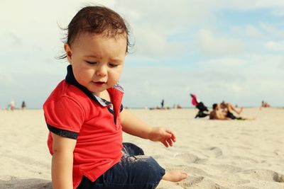 Cute boy sitting on sand at beach