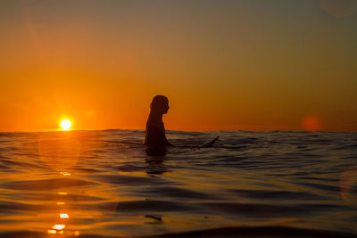 Silhouette woman swimming in sea against sky during sunset