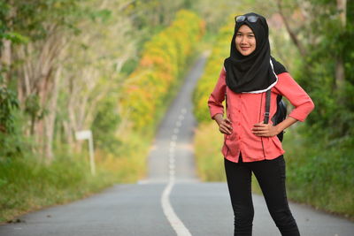 Portrait of young woman with hands on hip standing on road