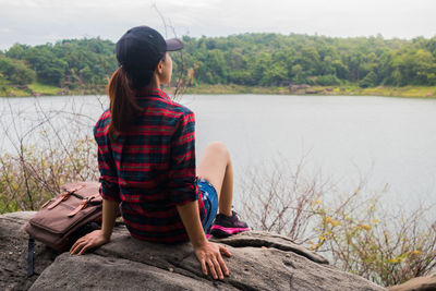 Rear view of woman sitting by lake against sky