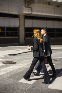Side view of businesswoman and businessman crossing road in city