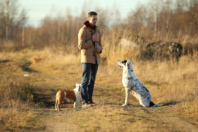 Man playing with dogs while standing on land against sky