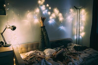 Woman lying on bed in illuminated room