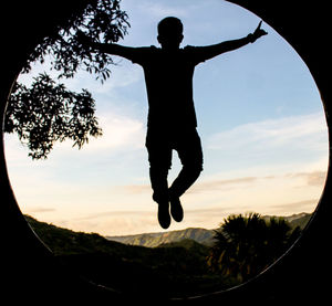 Silhouette man jumping on tree against sky