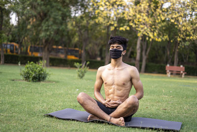 Full length of shirtless man sitting on tree