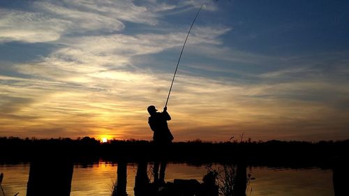 Rear view of silhouette man fishing at lake