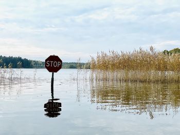 Information sign by lake against sky