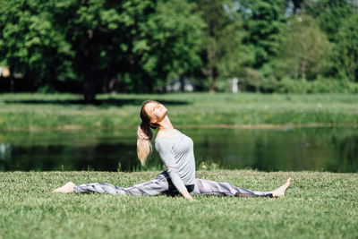 Full length of young woman exercising by pond on field