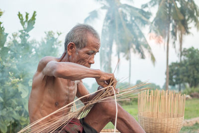 Shirtless senior man making straw basket