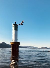 Lighthouse by sea against clear blue sky