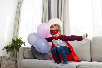 Portrait of smiling boy playing with balloons while sitting on sofa at home