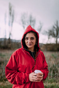 Portrait of young woman holding drink standing on field