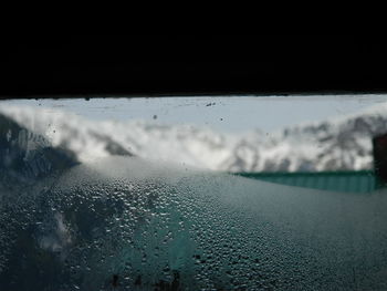 Close-up of wet window against sky