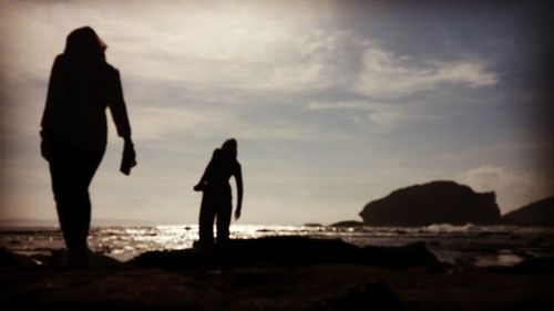 Silhouette people walking on beach against sky during sunset