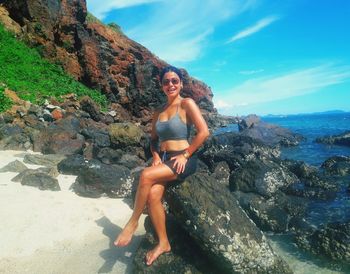 Full length portrait of woman sitting on rock by sea