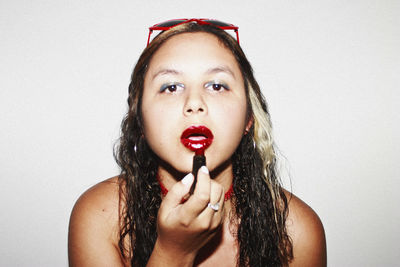 Close-up portrait of woman applying red lipstick against white background