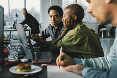 Multiracial business professionals discussing over laptop while working at office