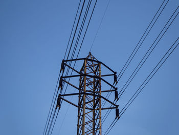 Low angle view of electricity pylon against clear blue sky