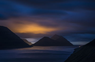 Scenic view of sea and mountains against cloudy sky at dusk