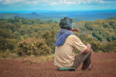 Rear view of man sitting on field against sky