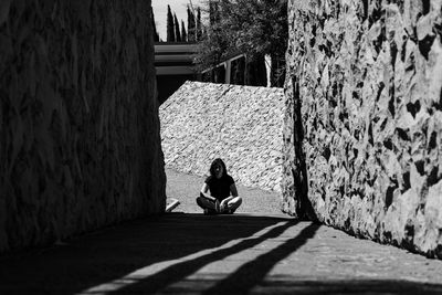 Woman sitting on footpath amidst wall