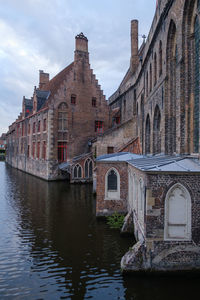 Arch bridge over river by buildings against sky