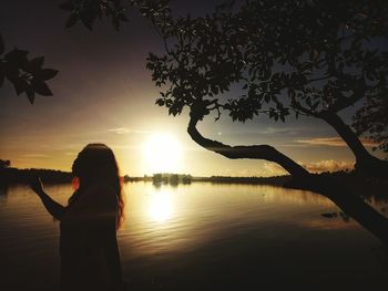 Silhouette woman standing by lake against sky during sunset