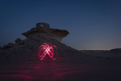 Low angle view of illuminated lighting equipment on desert against sky at night