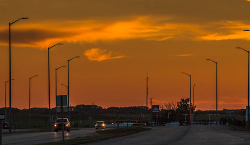 Cars on road against sky at sunset