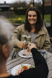 Happy woman raising toast with white wine and eating prawn sandwich